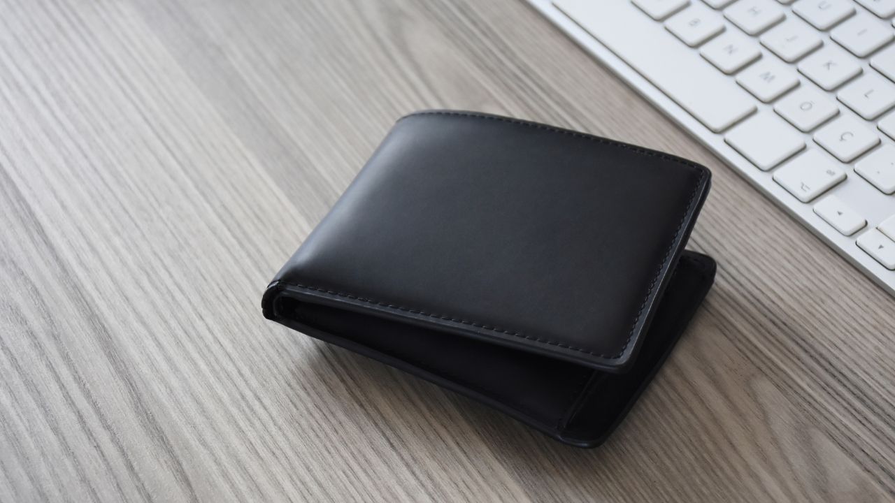 Sleek black men's wallet on a wooden desk near a keyboard.