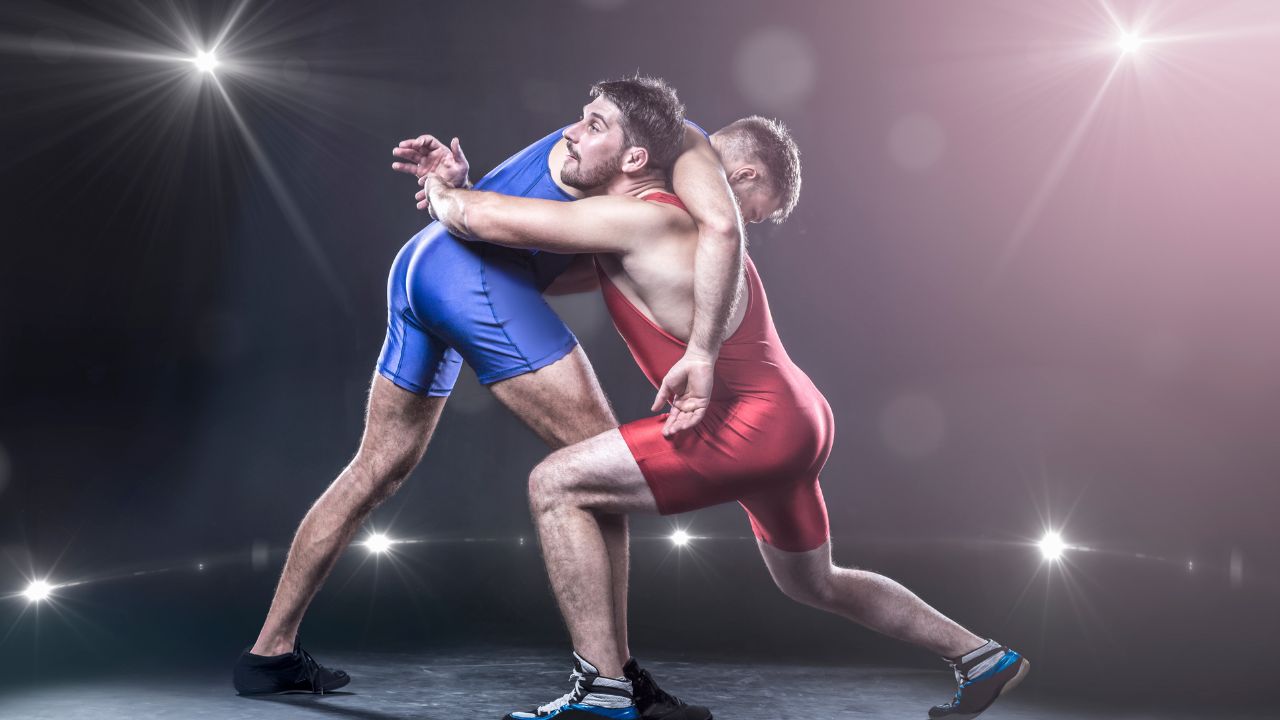 Two wrestlers in vibrant singlets competing under dramatic lighting.