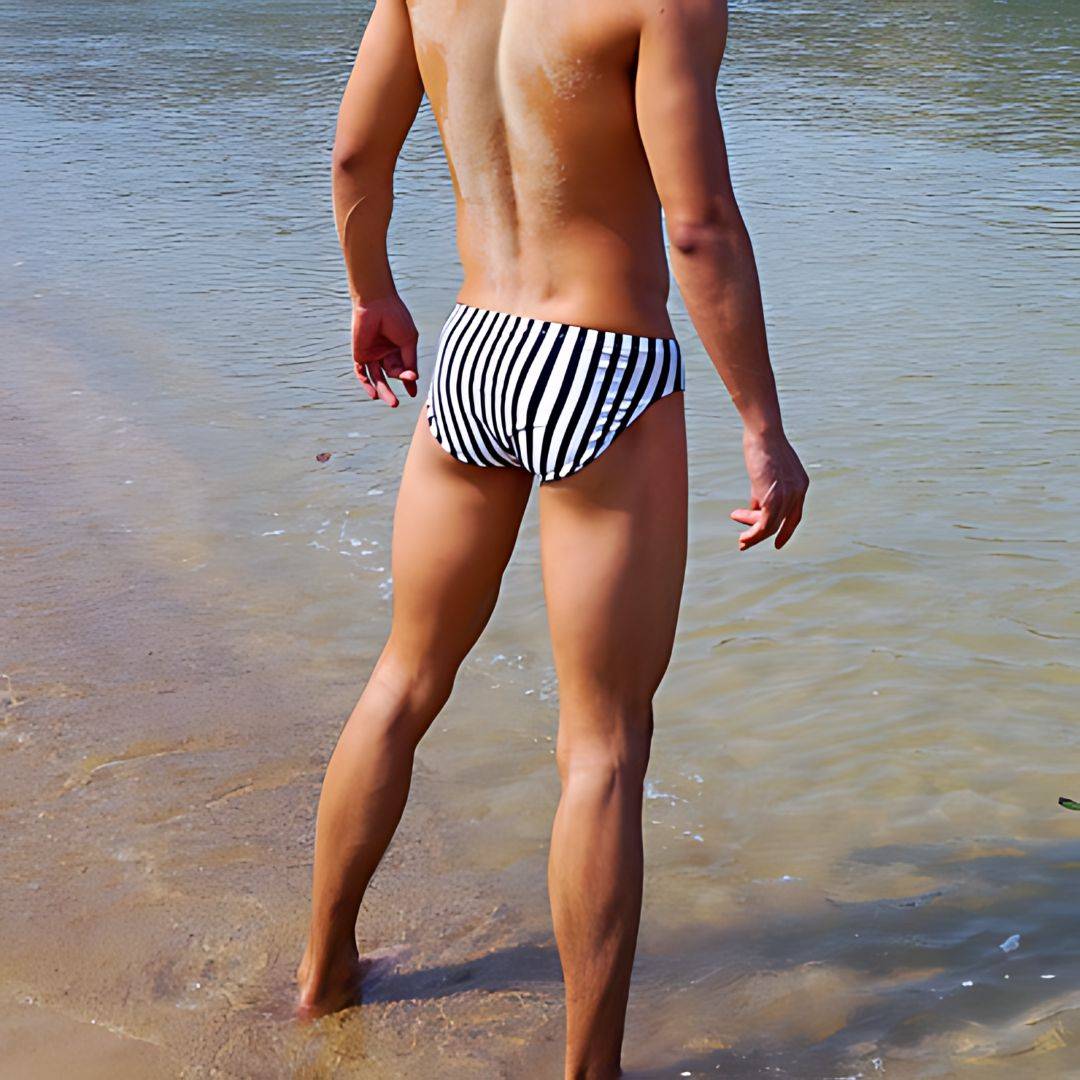 Back view of Black & White Vertical Stripe Swim Briefs worn by a man standing in shallow water at the beach.