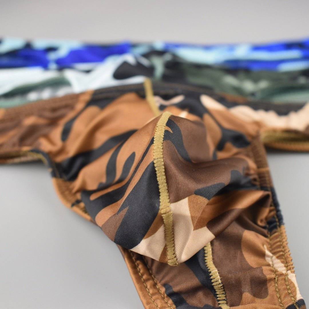 Close-up of brown camo thong's bulge pouch with other camo thongs in the background, highlighting the variety of colors.