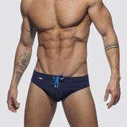 Front view of navy swim briefs featuring blue drawstring and rainbow detailing, made from a nylon-spandex blend.