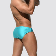 Men's shimmer low rise swim briefs in turquoise, back view emphasizing a sleek, snug fit and shimmering fabric.