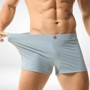 Close-up of men's light gray square cut swim trunks being stretched, showcasing the elasticity and high-quality quick-dry material.